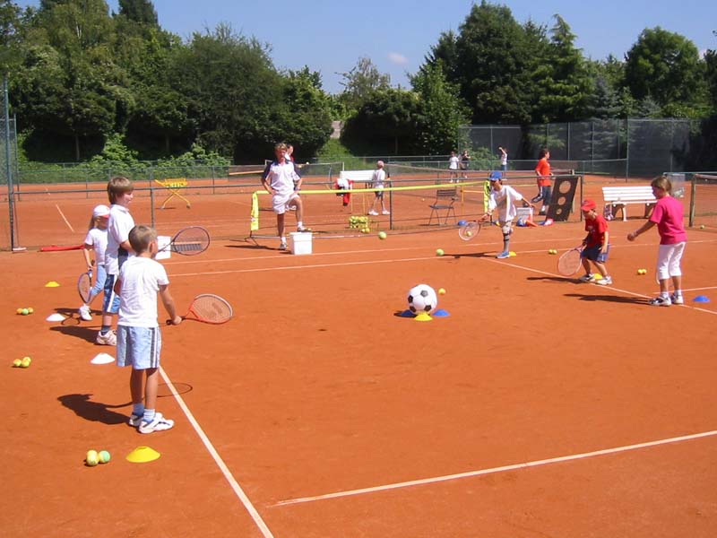 Kinder spielen Tennis auf einem roten Sandplatz mit Kindernetz - Gruppentraining der Kindertennisschule Goer