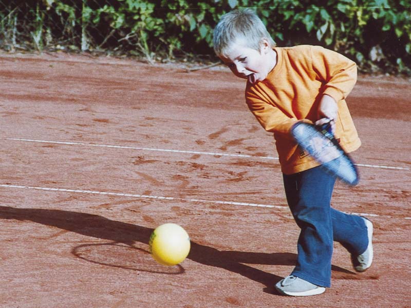 Kind schlaegt einen Tennisball auf dem Sandplatz der Kindertennisschule Goer in Koeln